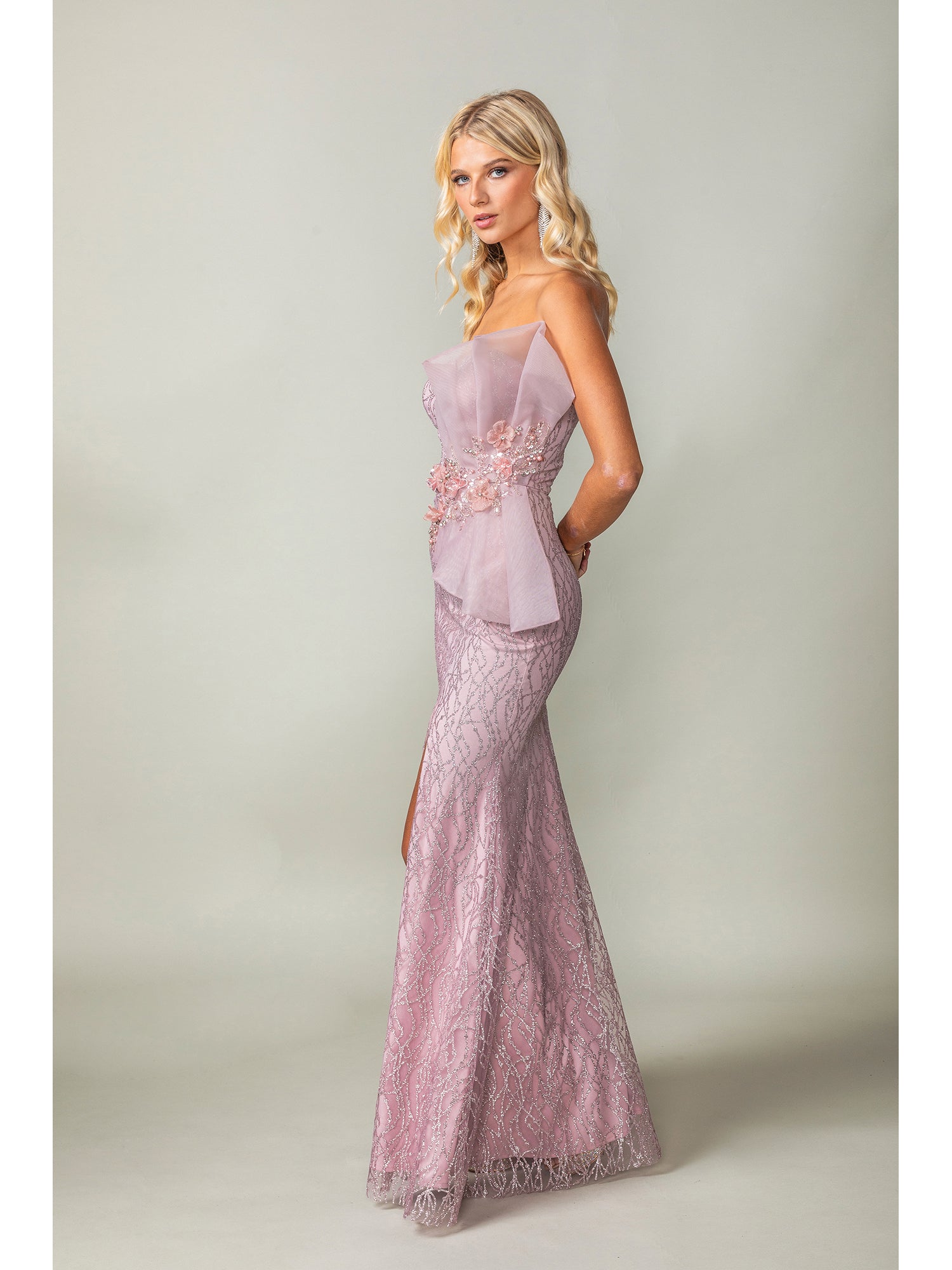 A woman stands in profile wearing the Side-Bow Strapless Long Glitter Prom Dress 4394, a shimmering strapless evening gown with a side bow detail, against a plain light background.